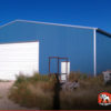 50x100x14 Commercial metal garage building 50 x 100 with blue walls and white trim, one roll up garage door and walk in door.