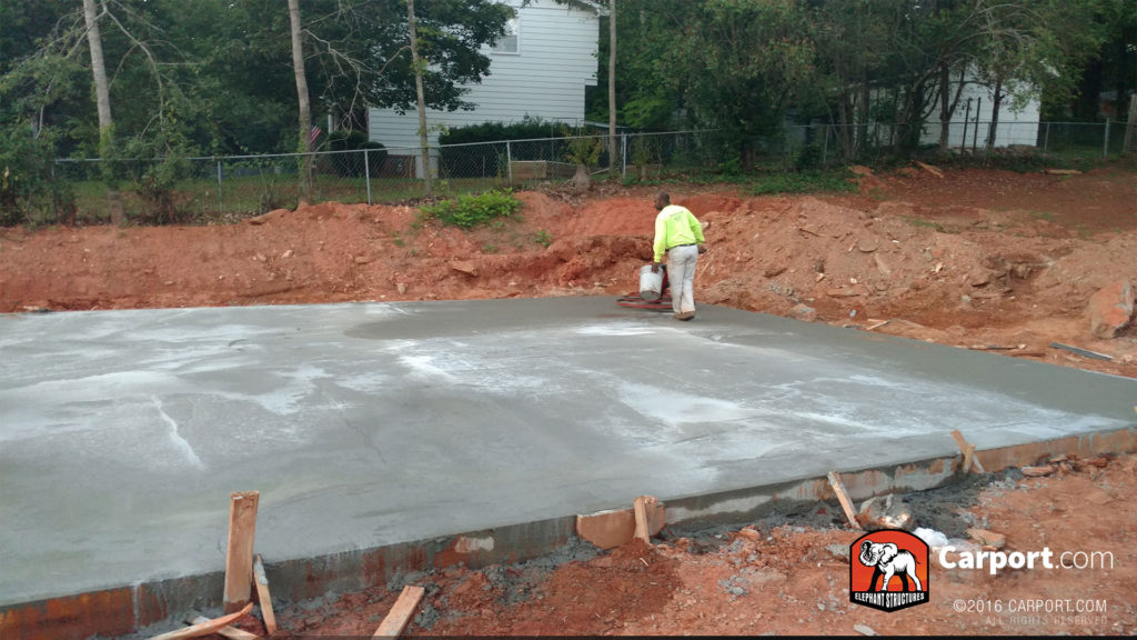 Concrete foundation is smoother out, and a worker carries a bucket across it.
