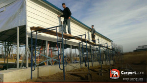 Installers using scaffolding to fasten paneling on to a carport. 